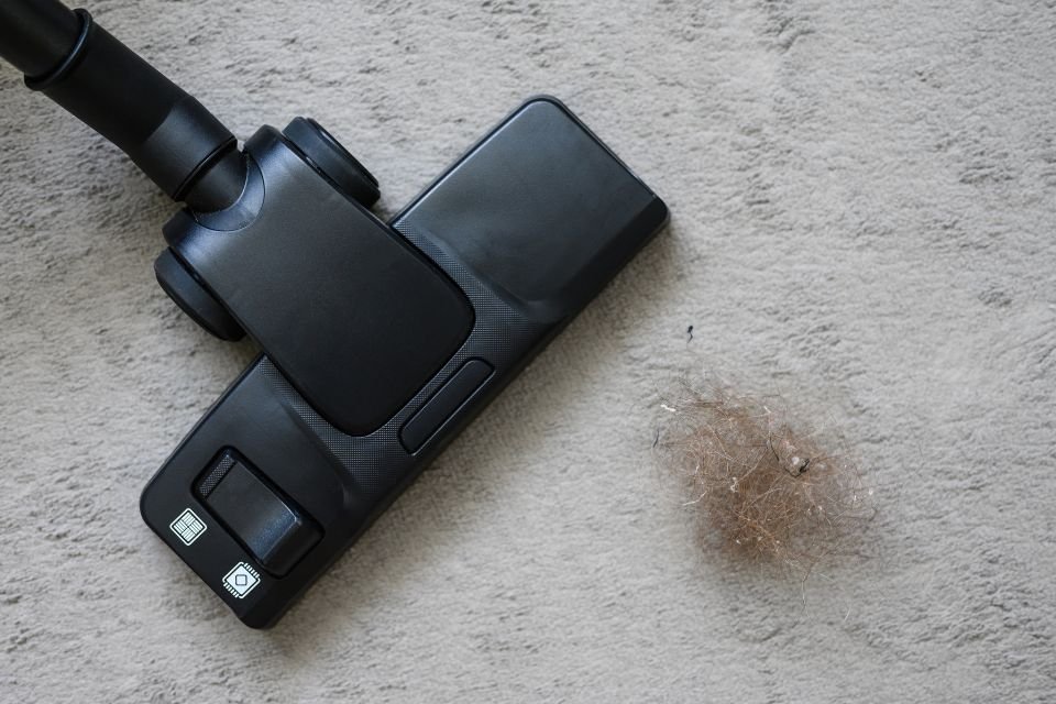 A vacuum cleaner on a carpet with a hair on the floor, symbolizing a carpet cleaning service in Las Vegas, NV.