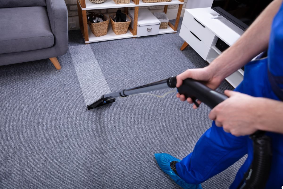A man wearing a blue shirt operates a vacuum cleaner on a carpet, ensuring it is clean and tidy.