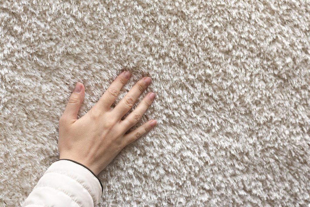 A hand reaching down to feel the fibers of a colorful carpet.