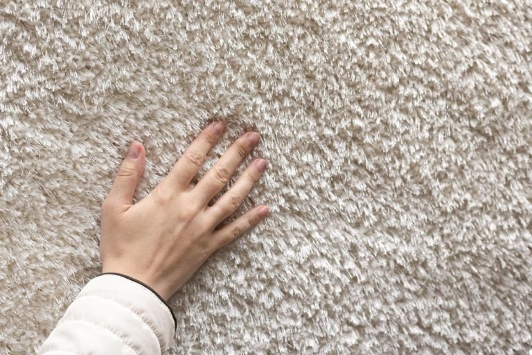 A hand reaching down to feel the fibers of a colorful carpet.