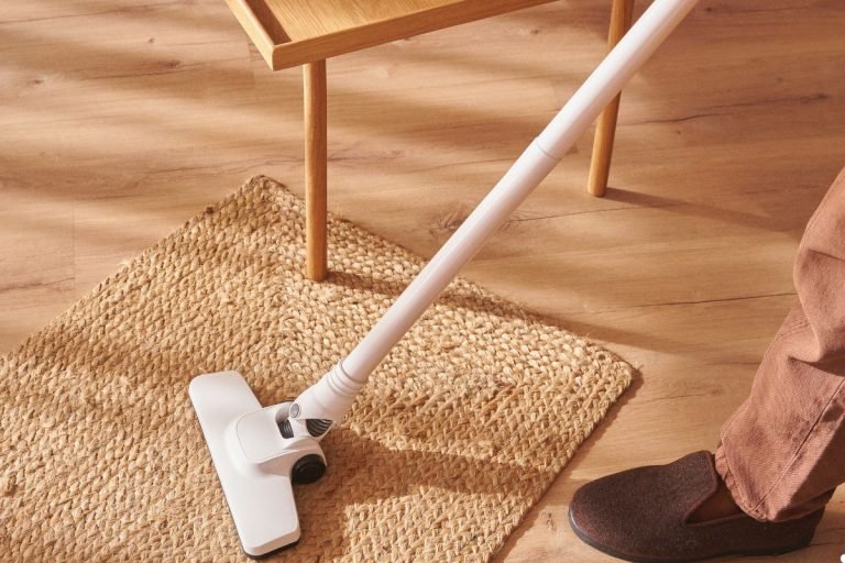 A person vacuuming a patterned rug, demonstrating household cleaning activity.